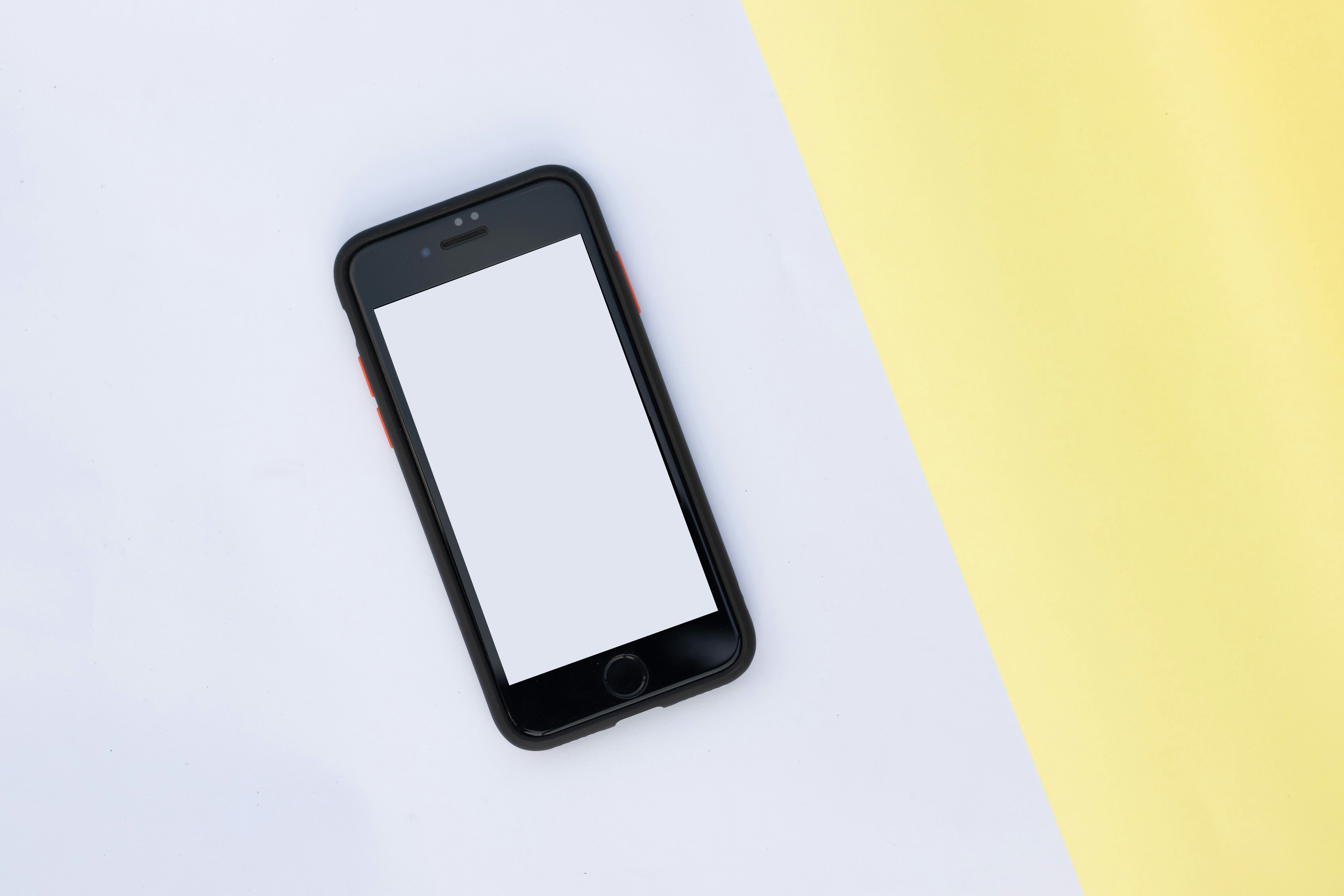 A Mobile phone with a blank screen mockup on yellow and white paper background.